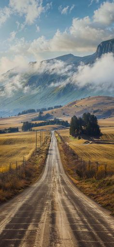 an empty dirt road in the middle of nowhere with mountains in the background and clouds