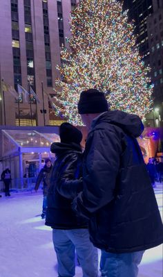 two people standing in front of a large christmas tree at rockefeller's ice rink