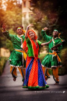 some people are dancing on the street in colorful outfits and headgear, with trees in the background