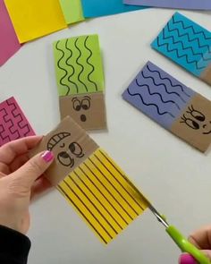 someone cutting out some paper with scissors on top of a white table covered in different colored papers