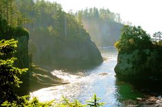 the sun shines through the trees and over the water as it flows between two large rocks