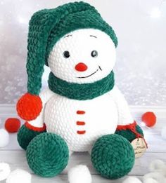 a knitted snowman sitting on top of a white table next to pom poms