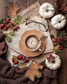 a cup of coffee sitting on top of an open book next to autumn leaves and pumpkins