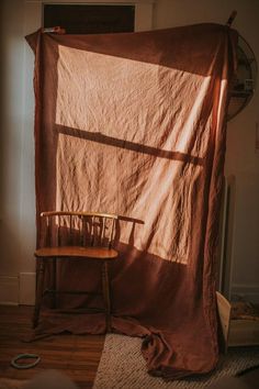 a chair sitting in front of a window covered by a blanket on top of a wooden floor