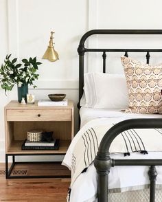 a black metal bed frame with white sheets and pillows in a small bedroom, next to a wooden nightstand