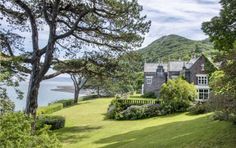 a large house sitting on top of a lush green hillside next to the ocean and mountains