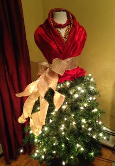 a mannequin dressed up as a christmas tree in front of a red curtain