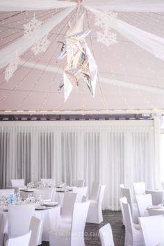 a banquet room with white tables and chairs covered in snowflakes hanging from the ceiling