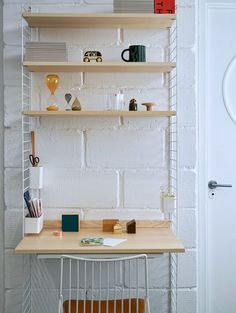 a white brick wall behind a desk with shelves on it and various office supplies sitting on top of it