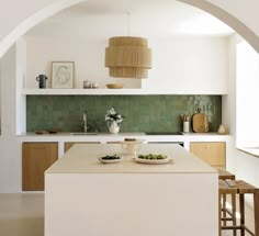 a white kitchen with green tiles on the backsplash and wooden stools in front of it