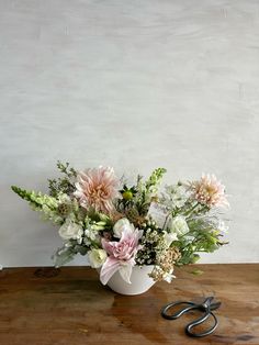 a bouquet of flowers in a white vase on a wooden table with scissors next to it