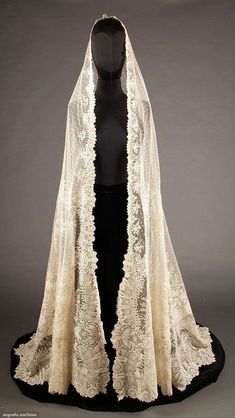 an antique white lace wedding veil with black velvet headpiece and cape on display in front of a mannequin