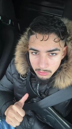 a man in a car gives the thumbs up sign with his hand and wearing a fur collar