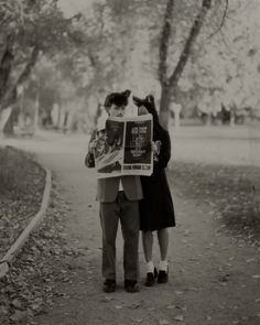 a man and woman walking down a path with a newspaper in their hands while holding each other's arms