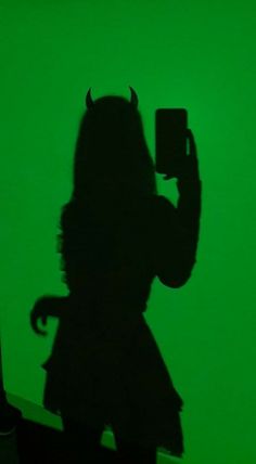 the shadow of a person holding a cell phone in front of a green wall with a devil on it