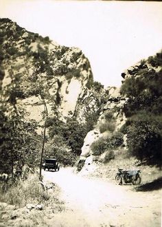 an old black and white photo of two motorcycles on a dirt road with mountains in the background