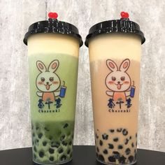 two iced drinks with bunny and cheesy milkshakes on them are sitting next to each other