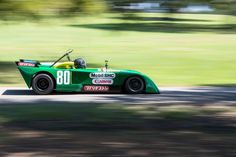 a green race car driving down a road with trees in the backgrouds