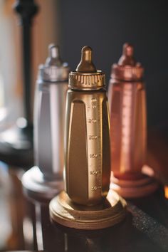 the baby bottle is on top of the table next to two other bottles, one gold and silver