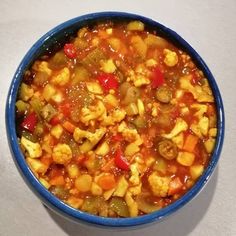 a blue bowl filled with food sitting on top of a white countertop next to a spoon