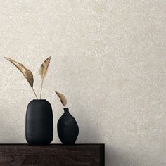 two black vases sitting on top of a wooden table next to a wallpaper