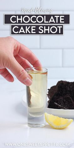 a hand dipping a piece of chocolate cake into a glass with ice and lemon wedges