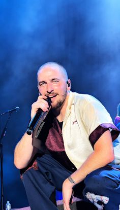 a man holding a microphone up to his mouth while sitting in front of a microphone