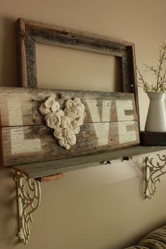 a wooden sign that says love hanging on a wall next to a vase with flowers