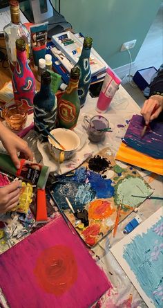 two people are painting on canvass at a table with bottles and other art supplies