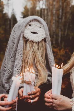 two women holding candles in their hands with the woman's face obscured by her hood