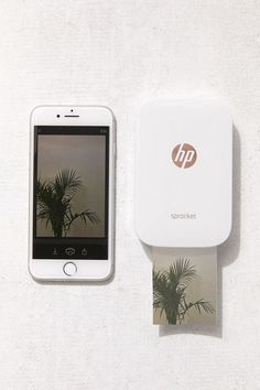 a cell phone sitting next to a printer on top of a white wall with a palm tree