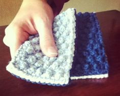 a hand is holding two crocheted dishcloths on a table