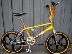 a yellow bicycle parked next to a metal wall with black rims and spokes