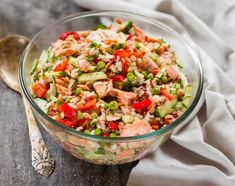 a salad in a glass bowl on top of a wooden table next to a spoon