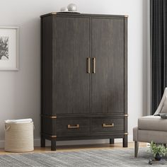 an armoire in a living room next to a gray chair and white wall with pictures on it