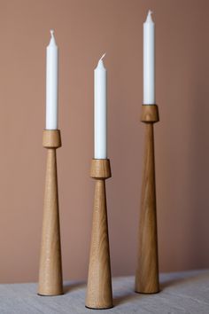 three wooden candlesticks on a table with one candle in between them and the other turned upside down