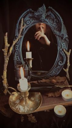 a woman is looking at her reflection in a mirror with candles on the table next to it