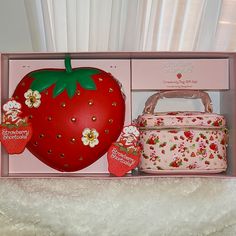 a strawberry shaped cake in a pink box next to two matching handbags and a purse