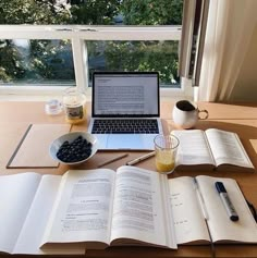 an open book sitting on top of a wooden desk next to a laptop computer and cup of coffee