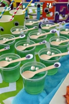 green cups with googly eyes and wooden spoons in them on a tablecloth