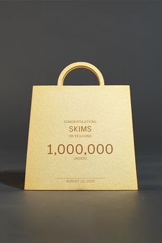 a gold shopping bag with the words skims on it, sitting on a table