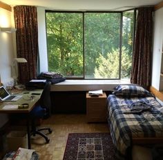 a bedroom with a bed, desk and window overlooking the trees outside in front of it