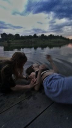 two people are sitting on the dock with their feet in the water and one person is reaching for something