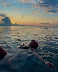 a person floating in the water at sunset with their head above the water's surface