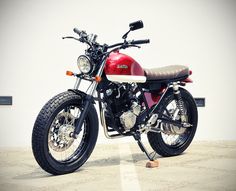 a red and black motorcycle parked in front of a white building with no one on it