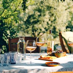 a table with wine glasses, plates and food on it in front of some trees