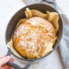 a person holding a loaf of bread in a pan with the words no knead honey oat crusty bread