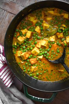 a pan filled with peas and tofu on top of a wooden table