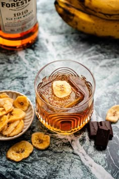 a glass filled with ice and banana slices next to a bowl of chocolate chips on a table