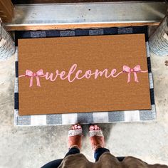 a welcome mat with pink bows and the word welcome is on top of a person's feet